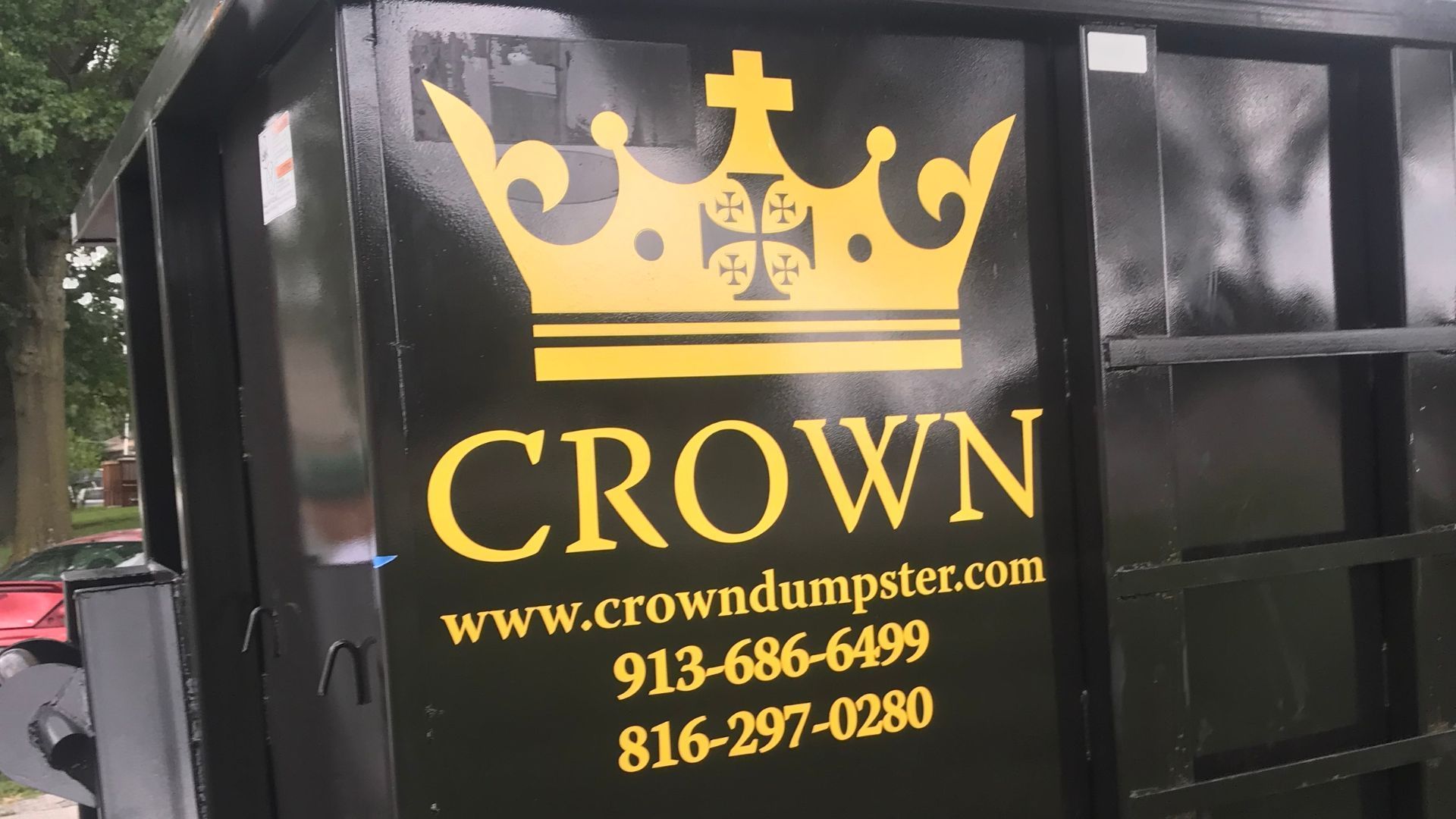 Black dumpster with a gold crown logo; reads 