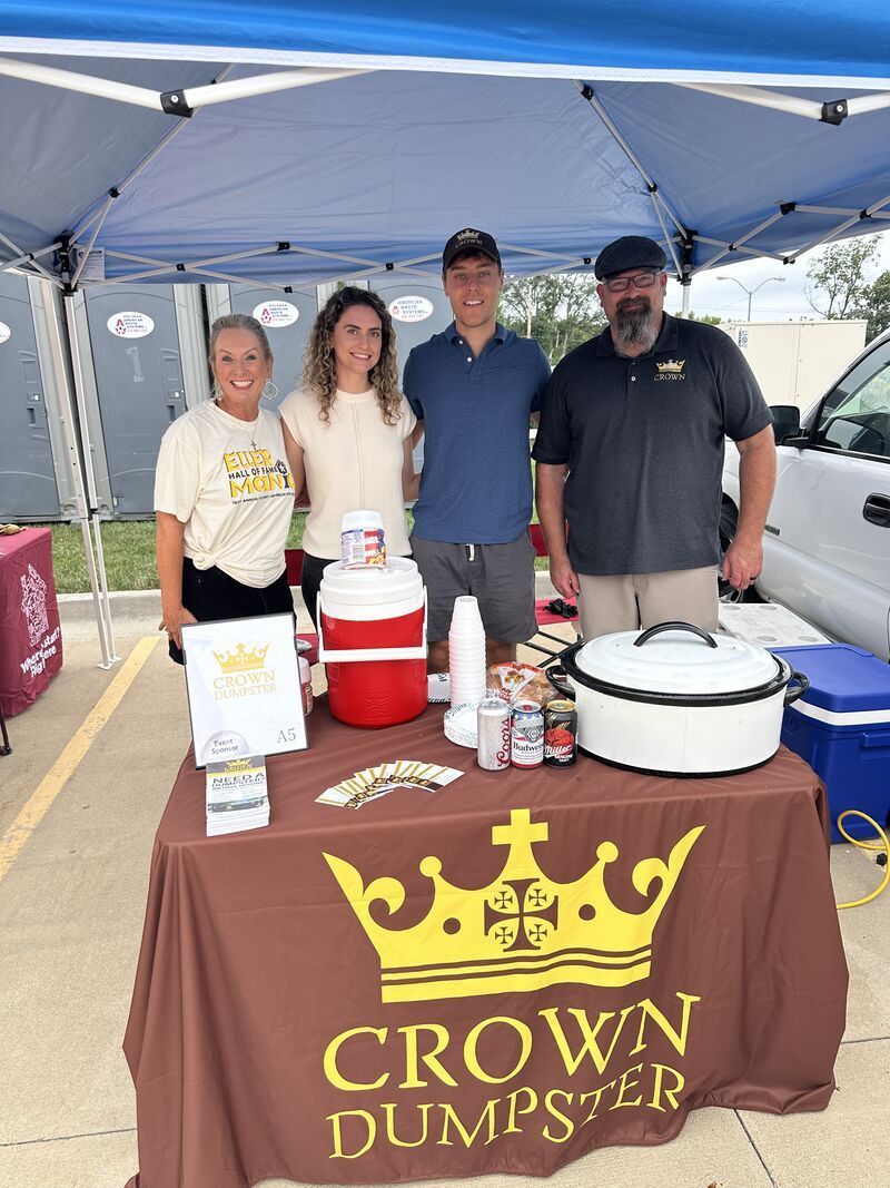 Four people stand behind a table with food, drinks, and a
