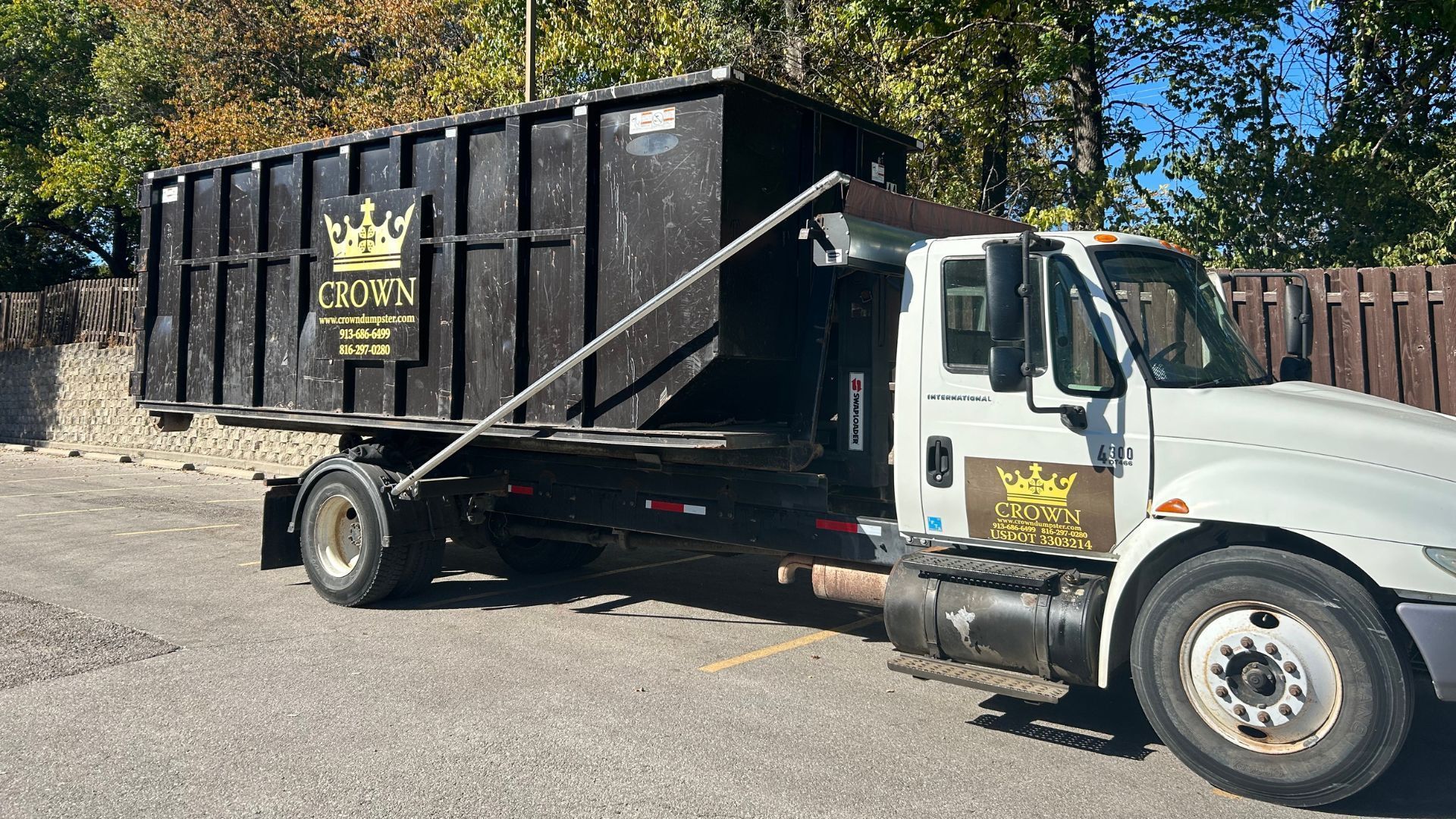 Black dumpster on a truck with gold logo, parked outdoors on asphalt.