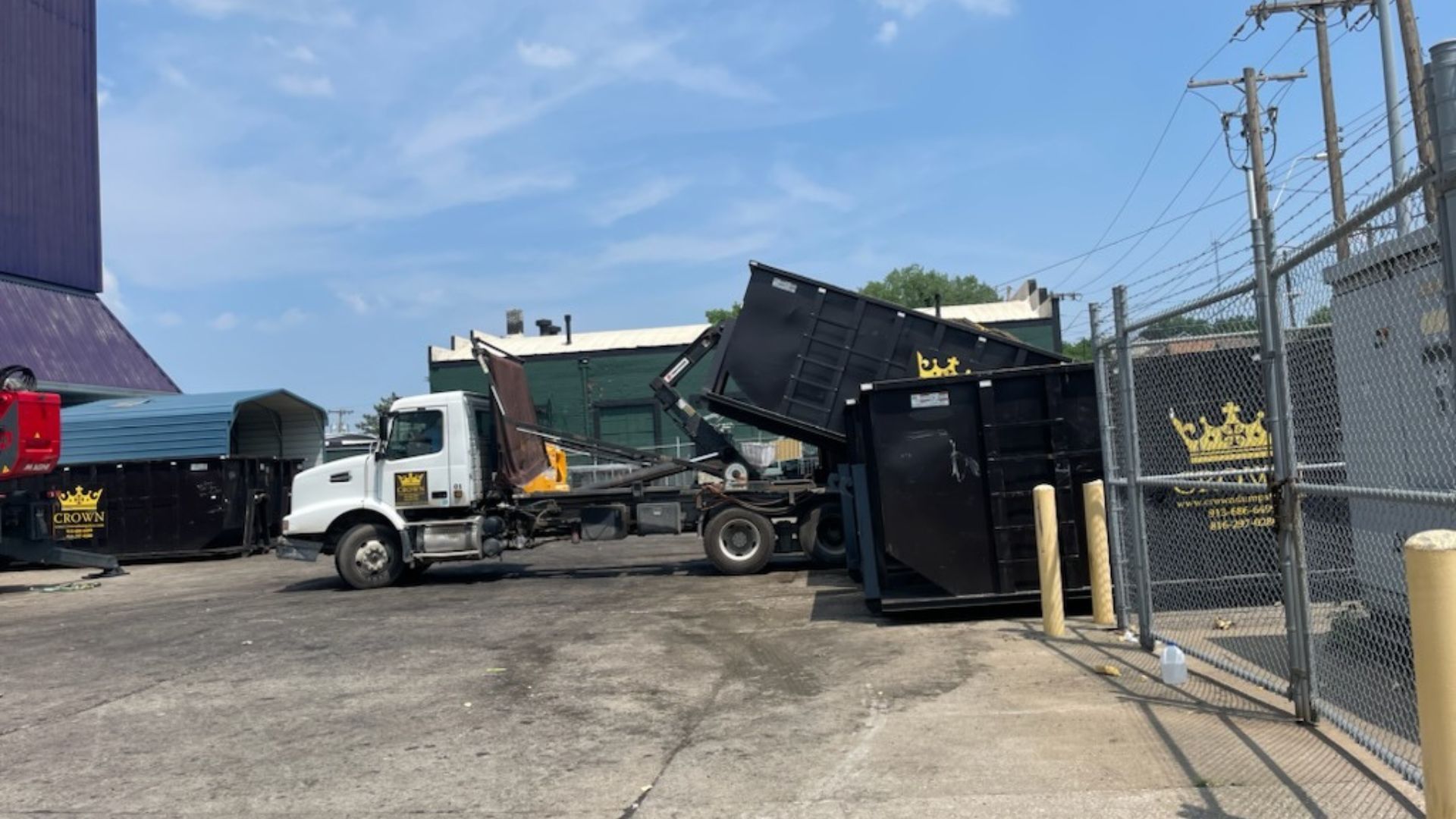 A truck with a dumpster lifting in an outdoor lot on a sunny day.