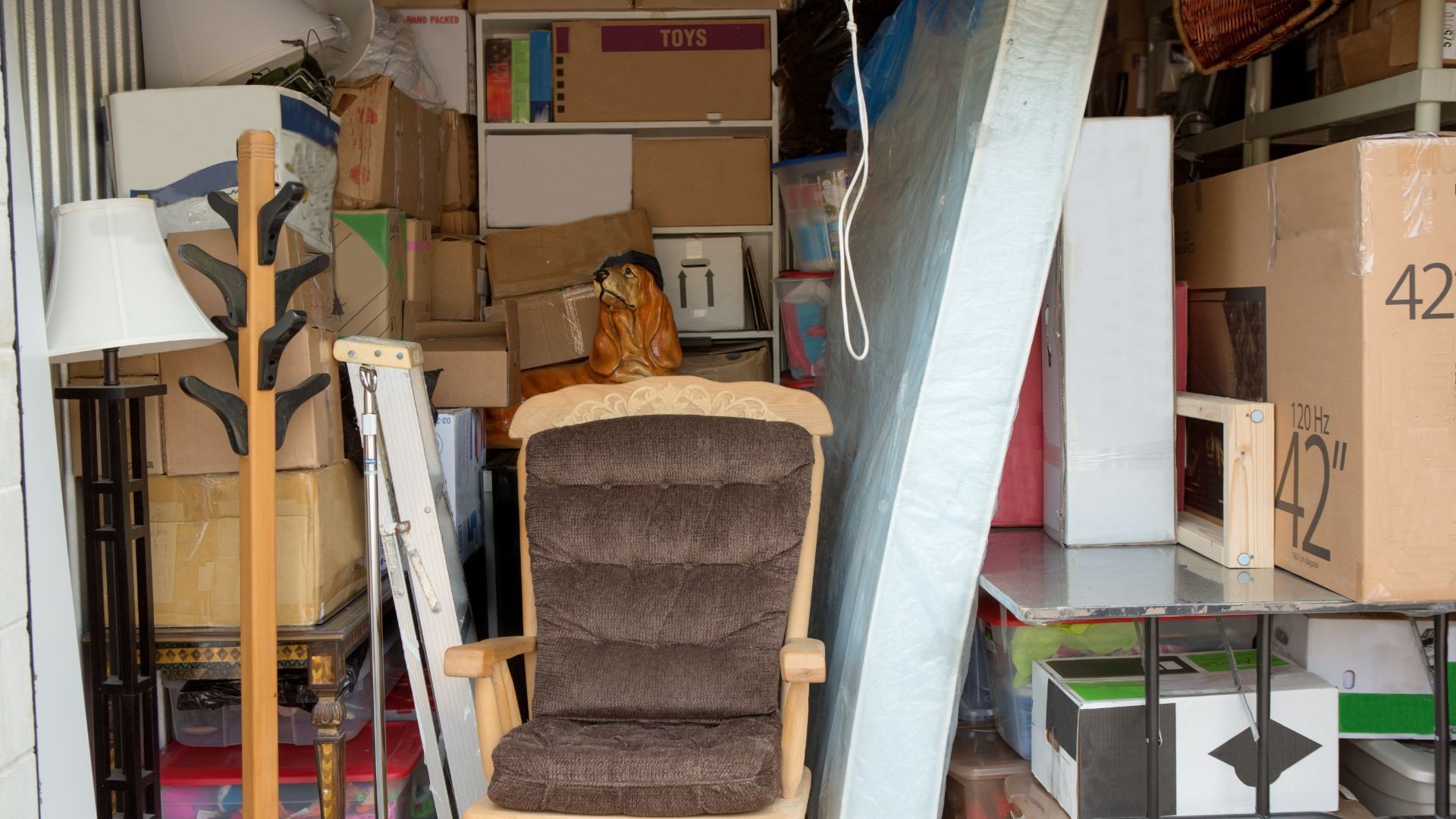 Storage unit filled with boxes, furniture, and a floor lamp.