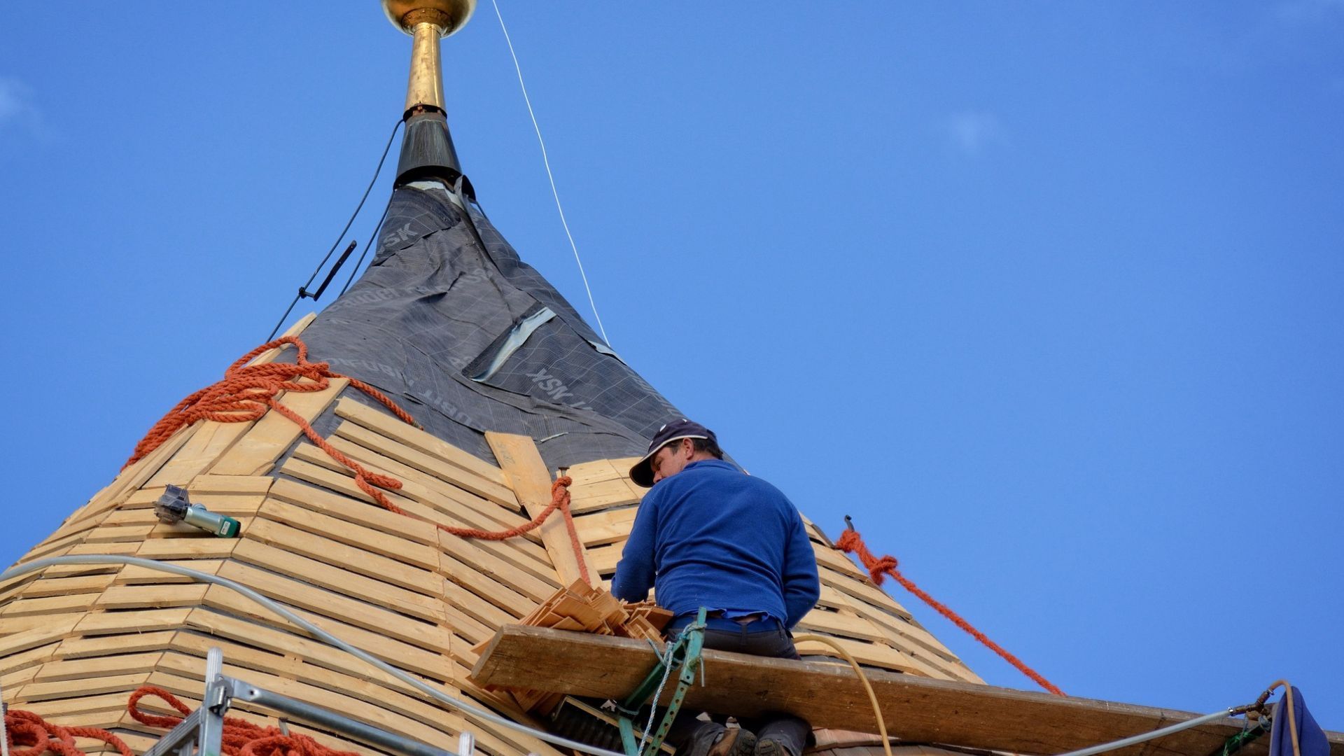 Roofer working on a wooden, rounded roof under a bright blue sky.