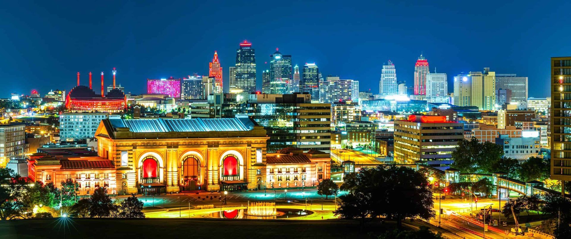 Nighttime view of Kansas City, Missouri skyline with illuminated buildings and Union Station in foreground.