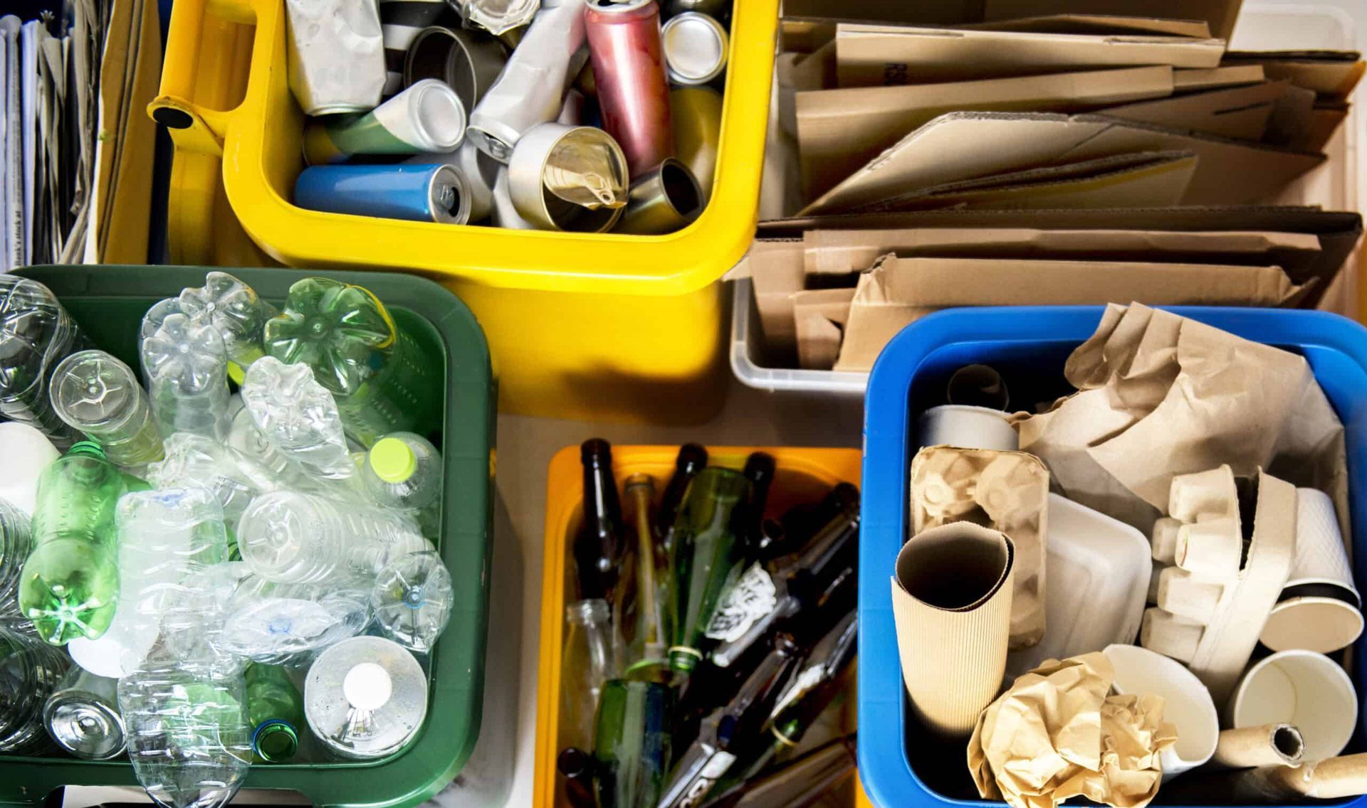 Recycling bins sorted by material: plastic, metal, glass, and paper/cardboard.