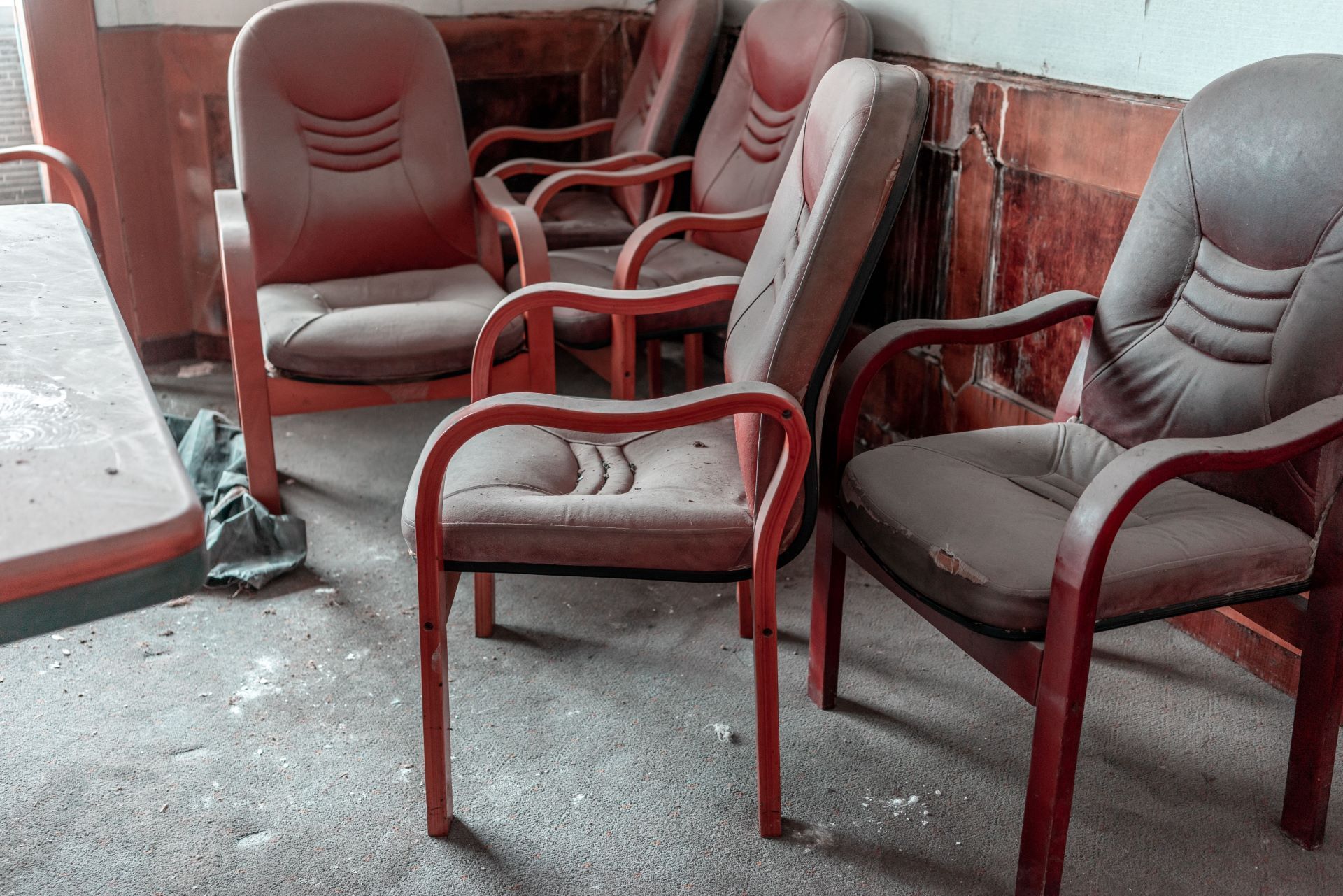 Dusty red chairs in a dilapidated room, likely abandoned, against a worn wall.