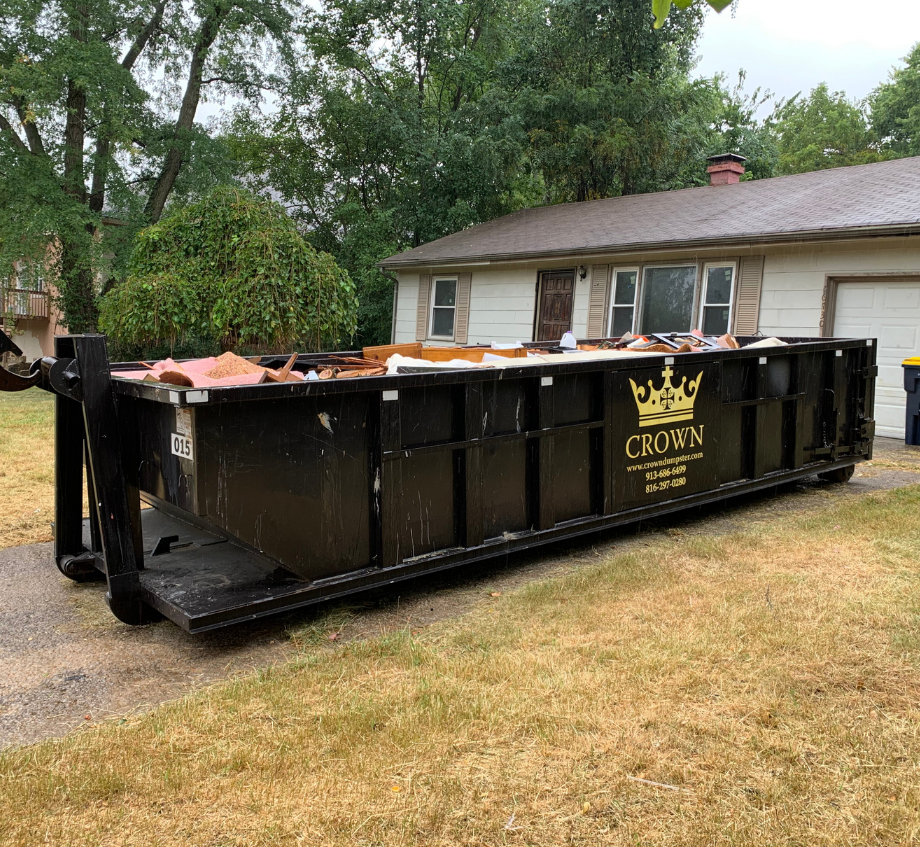 Black dumpster filled with debris in front of a house.