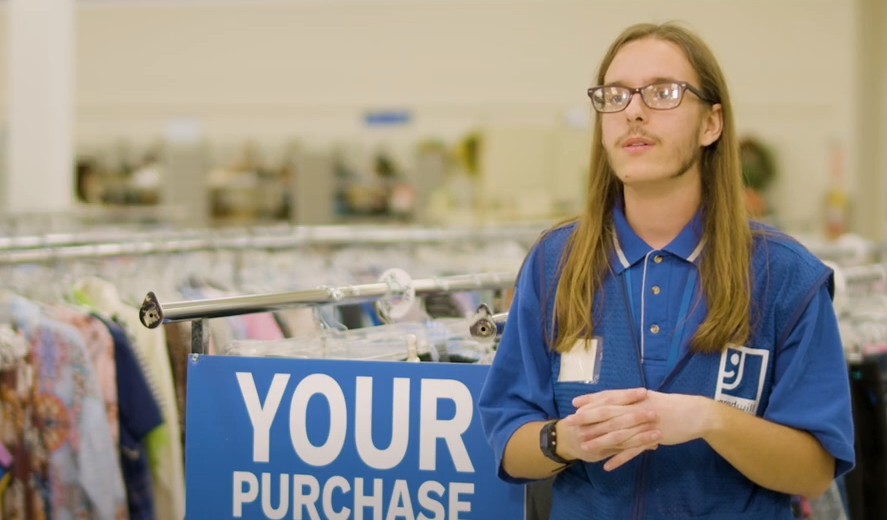 A man in a blue shirt is standing in front of a sign that says `` your purchase ''.