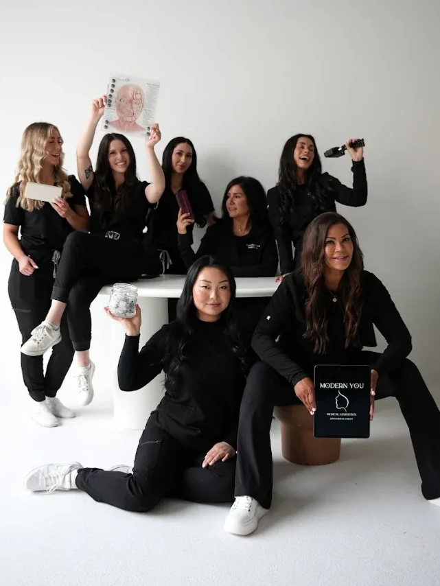 Group of women in black scrubs, smiling, holding items, posing in a studio.