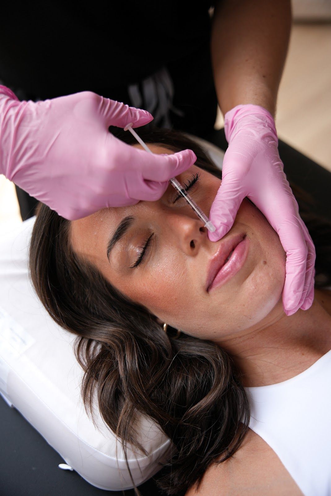 Woman receiving lip injection, practitioner wearing pink gloves injects with needle.