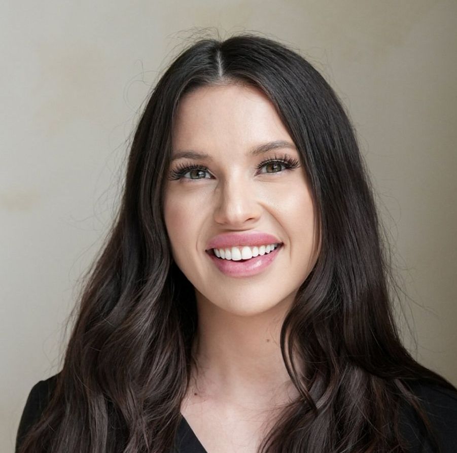 Woman with long dark hair smiling, wearing a black top.