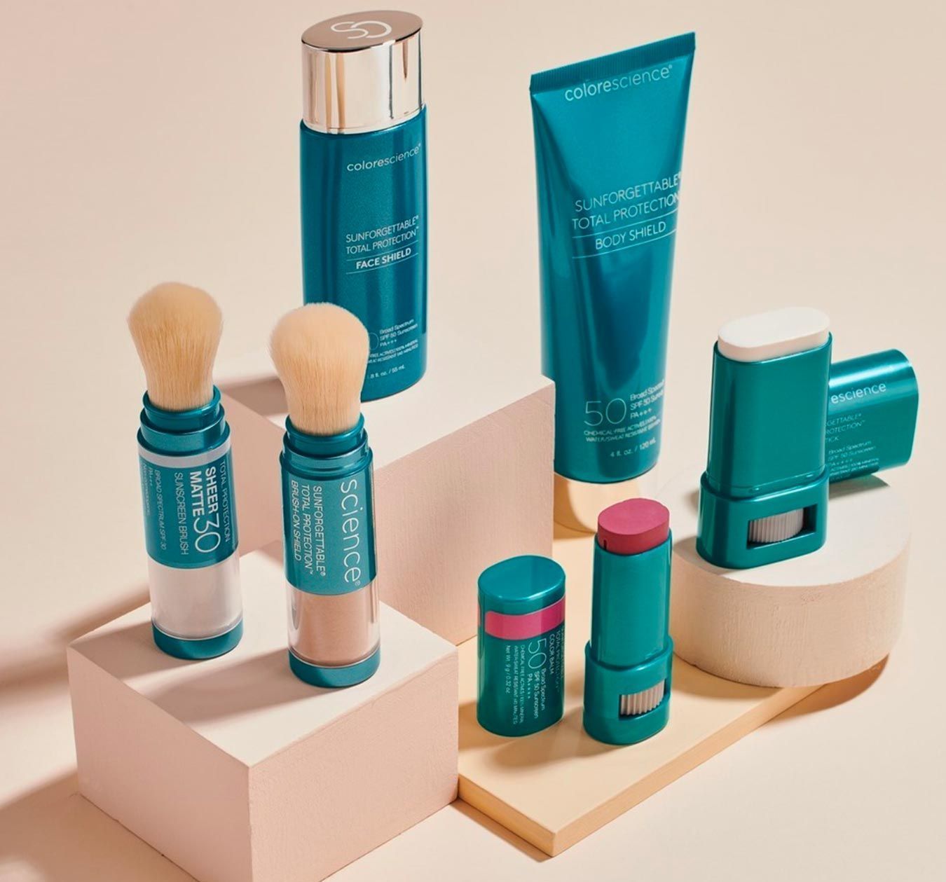 Colorscience Cosmetics in teal and white containers, including brushes, lotions, and sticks, on a peach and white surface.