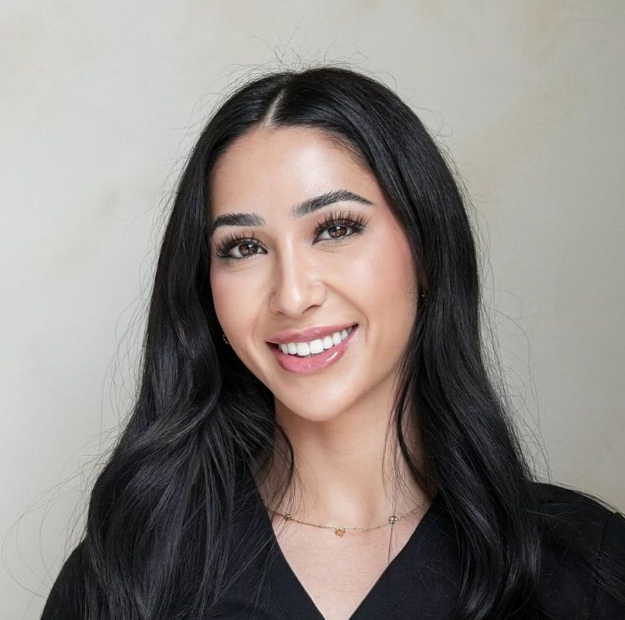 Woman with long black hair smiling; wearing a black top and gold necklace.