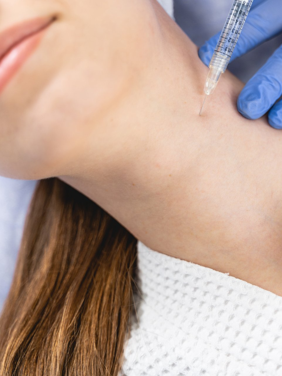 A medical professional in blue gloves administers an injection into a patient's neck area.