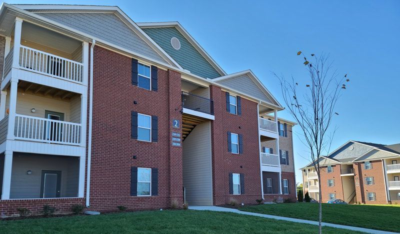 A large brick apartment building with balconies and a tree in front of it.