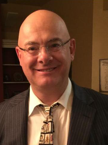A bald man wearing a suit and tie smiles for the camera