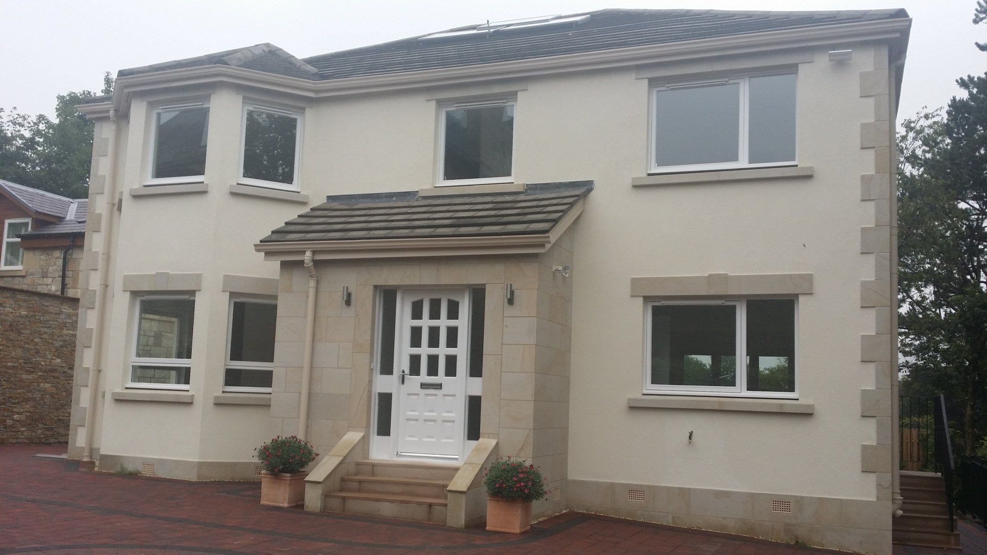 Dwupiętrowy dom ze stiuku z białymi wykończeniami, szarym dachem i małym gankiem nad białymi drzwiami.