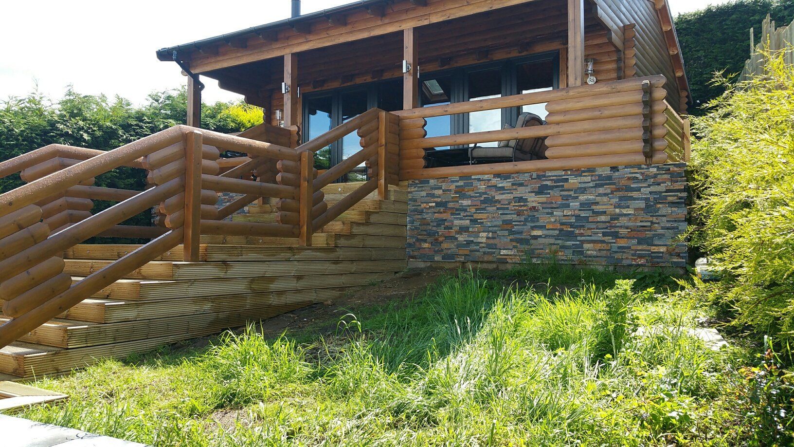 Drewniana chata z kamiennym fundamentem i schodami z bali, na trawiastym zboczu wzgórza.