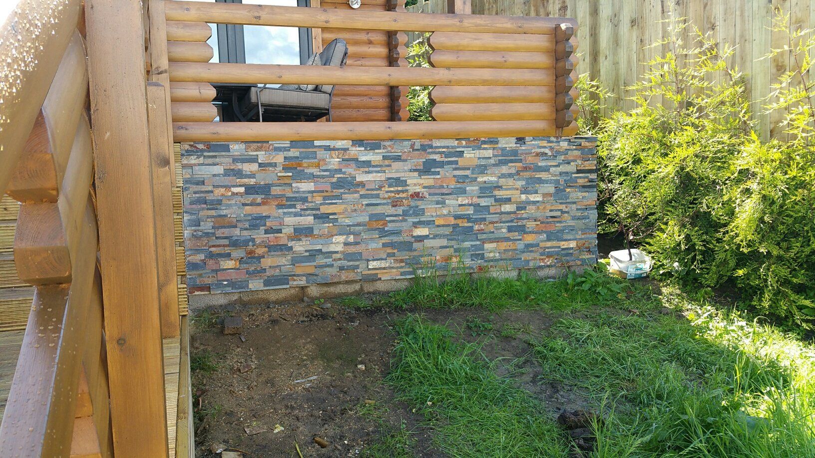 Kamienny mur pod drewnianym pokładem z trawą z przodu.