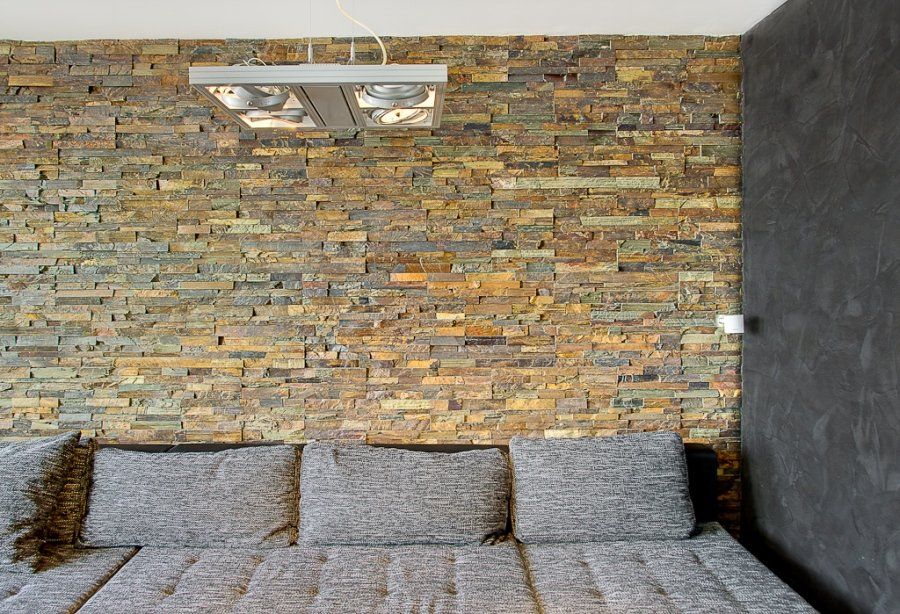 Ściana kamienna z sofą i kwadratowymi poduszkami; wpuszczane oświetlenie.