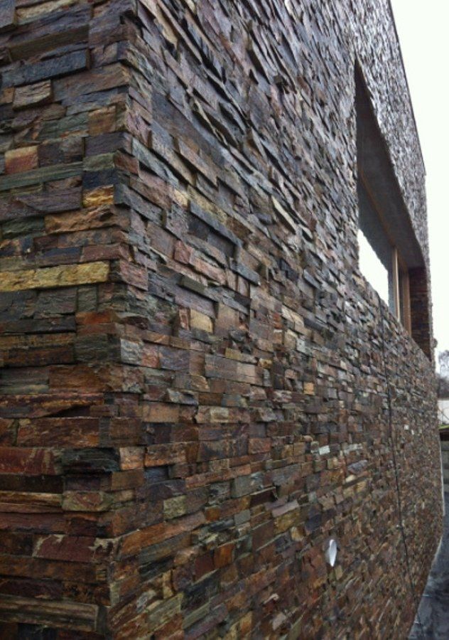 Zewnętrzna część budynku z fasadą wykonaną z teksturowanego kamienia w odcieniach brązu, szarości i złota.