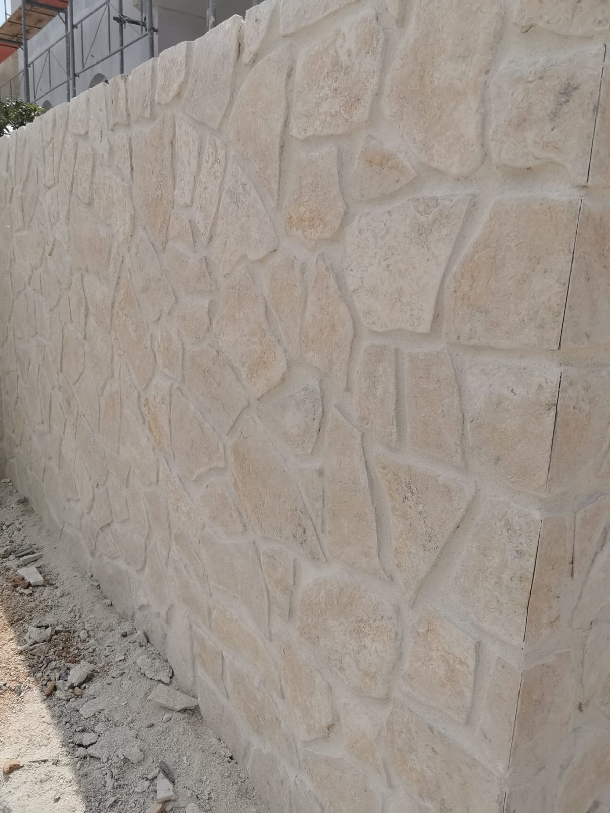 Mur kamienny z jasnobeżowych kamieni o nieregularnych kształtach i jasnoszarej zaprawy.