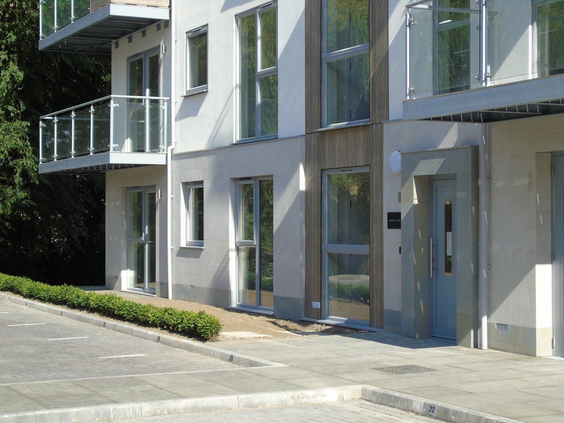 Wygląd zewnętrzny nowoczesnego budynku mieszkalnego z balkonami, szklanymi balustradami i wejściem.