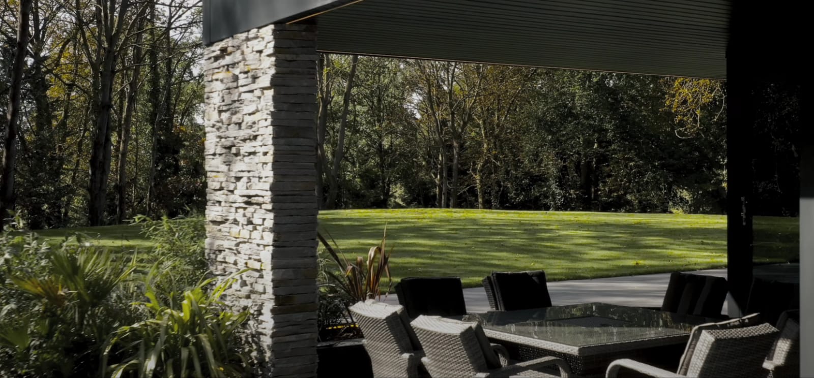 Jadalnia na świeżym powietrzu z kamiennym filarem i trawnikiem w tle.