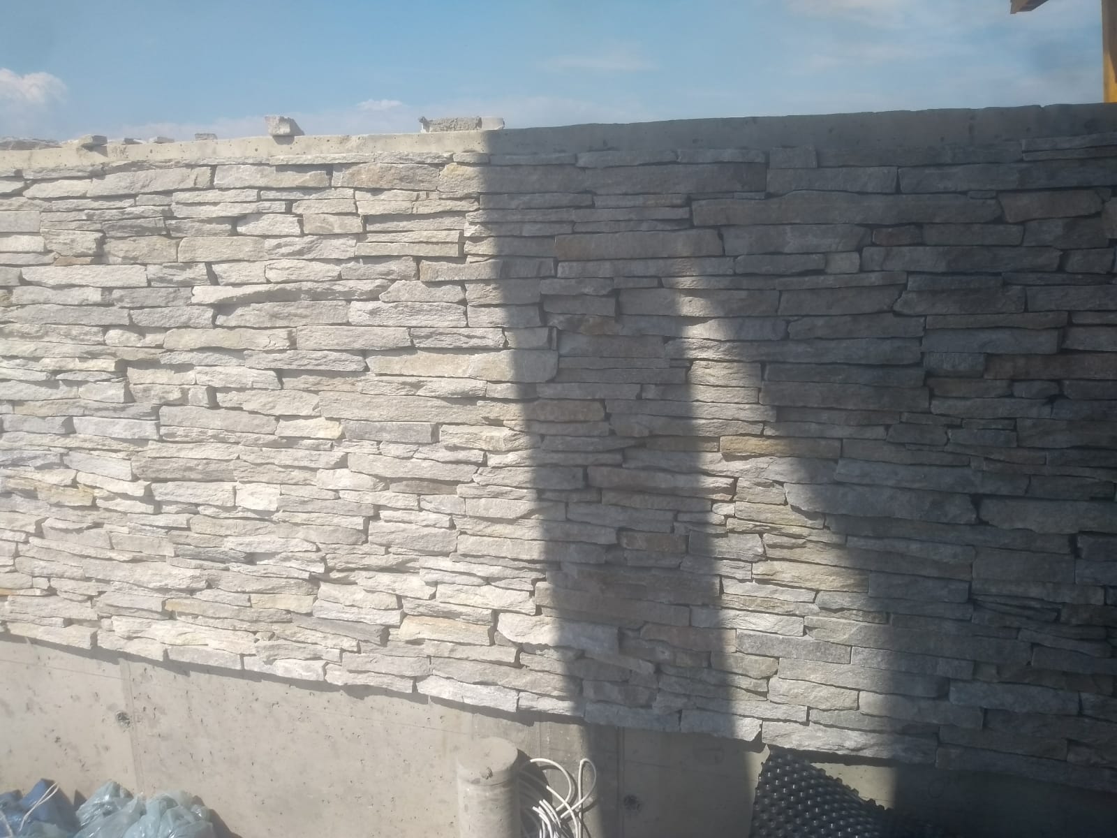 Ściana wyłożona kamieniem z poziomymi, jasnoszarymi, prostokątnymi kamieniami. Cień pada na ścianę.