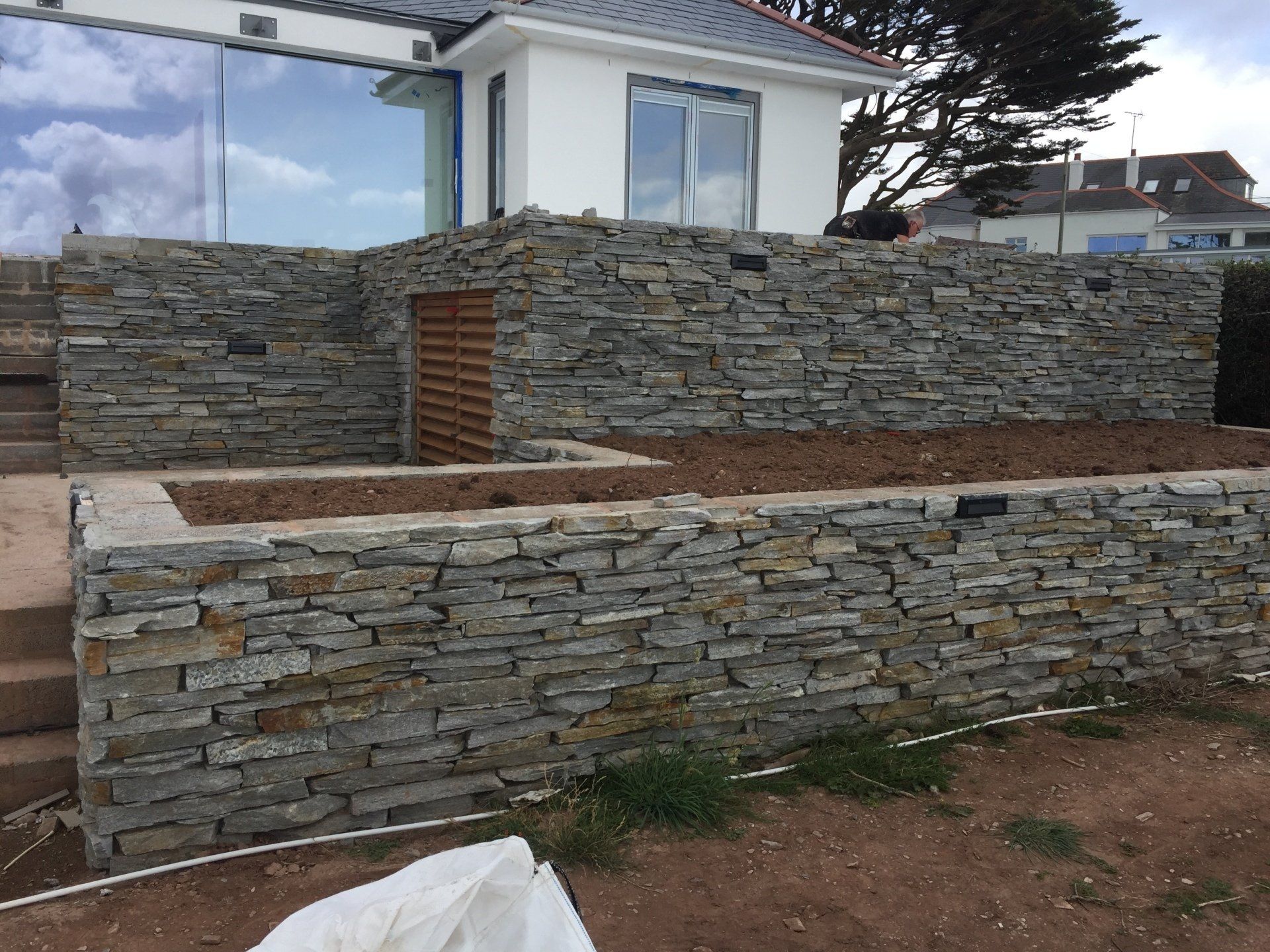 Kamienne mury oporowe ze schodami i budynkiem w tle.