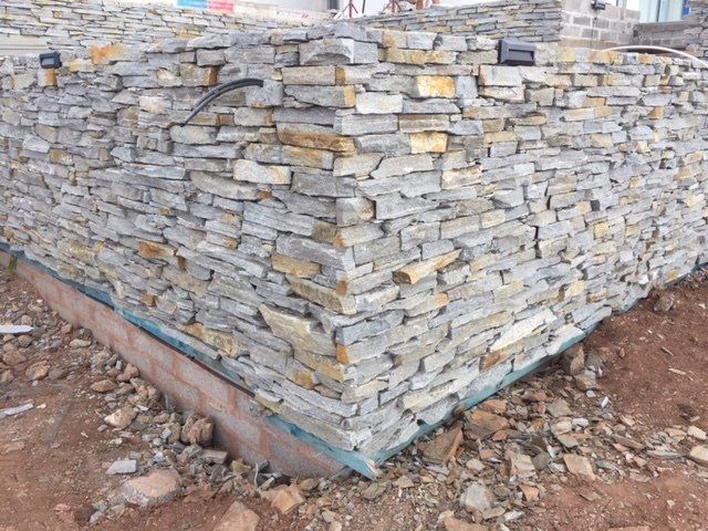 Kamienna okładzina na narożniku budynku w budowie. Szare i brązowe kamienie ułożone jedna na drugiej.