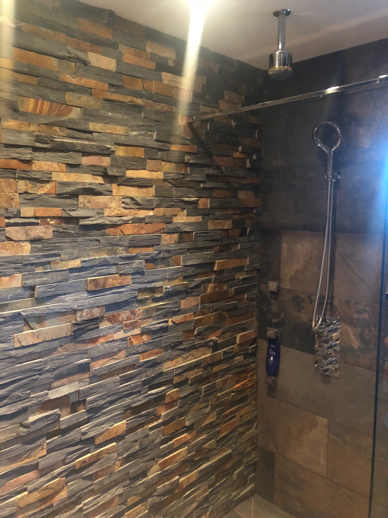 Prysznic ze ścianą wykończoną płytkami kamiennymi, szklaną kabiną i srebrnymi elementami wyposażenia.