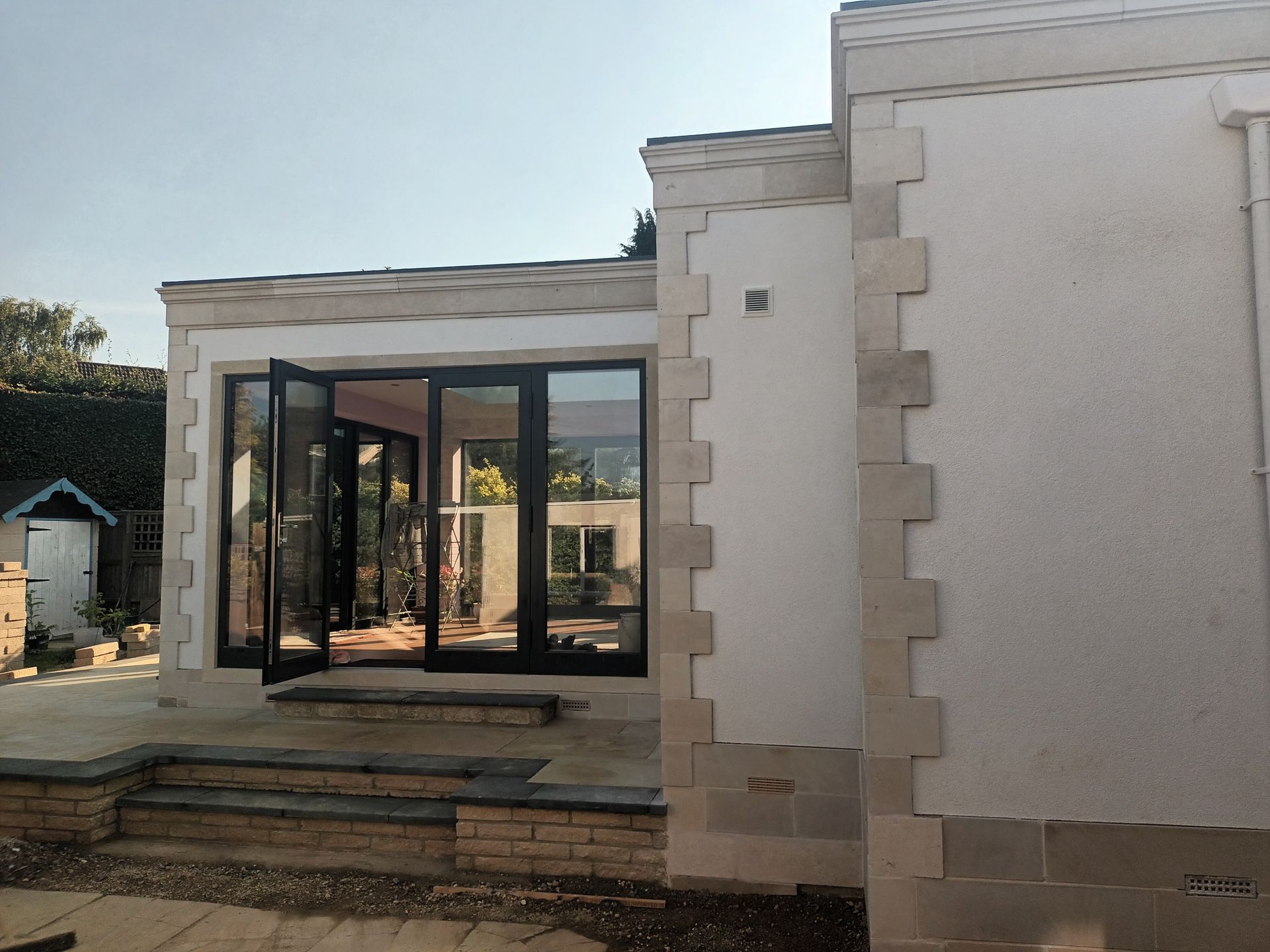 Widok zewnętrzny białego, stiukowego budynku z czarnymi, szklanymi drzwiami i kamiennymi wykończeniami.