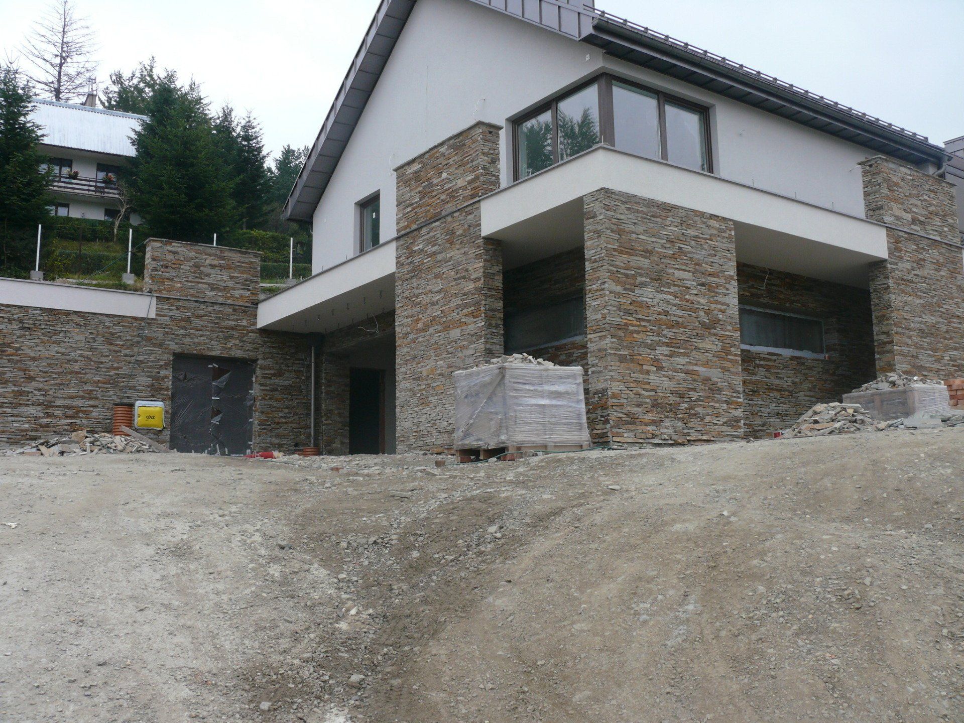 Nowoczesny dom w trakcie budowy z kamienną elewacją i żwirowym podwórkiem.
