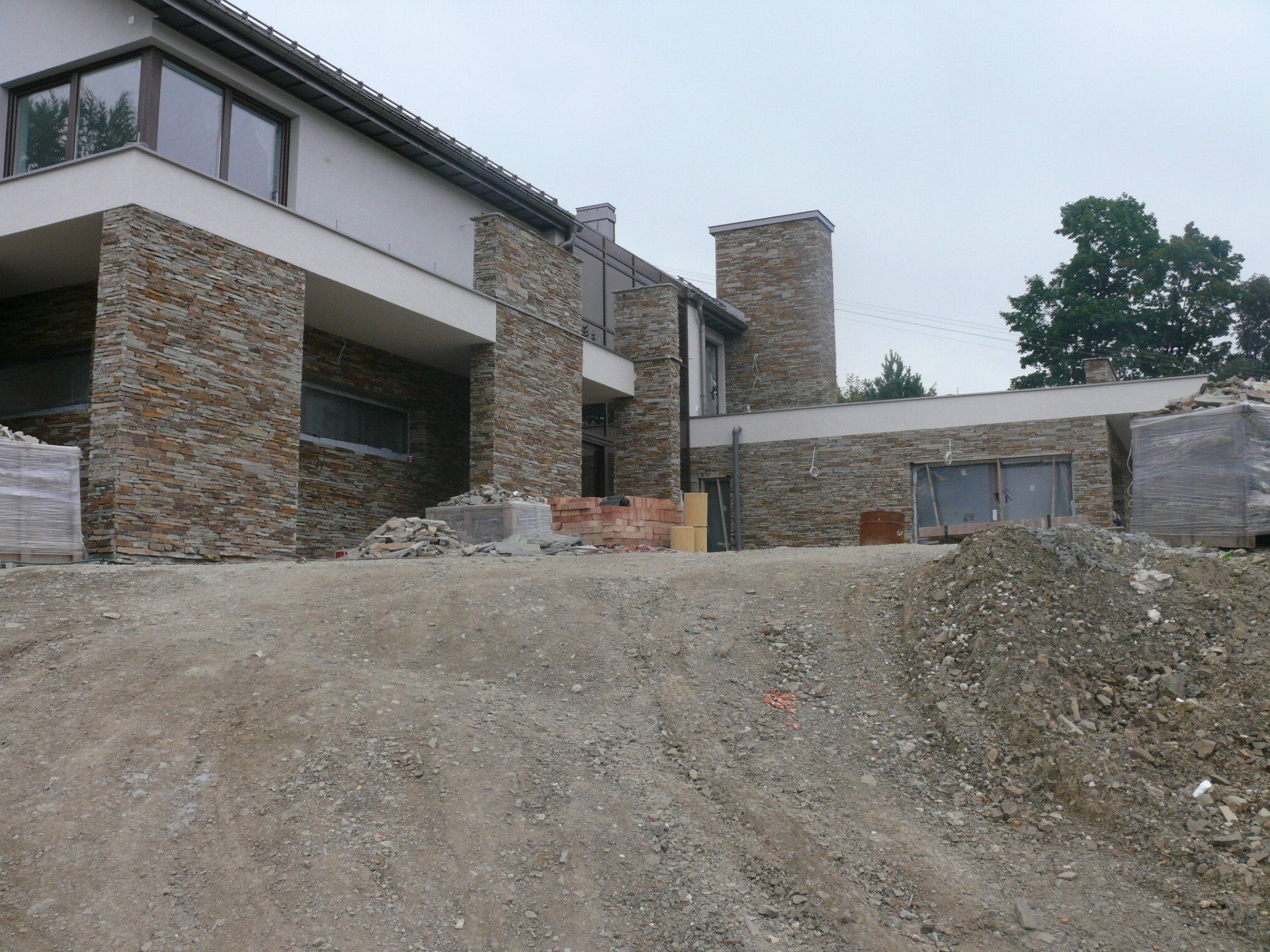 Nowoczesny dom w budowie z kamienną fasadą, gruzem i zachmurzonym niebem.