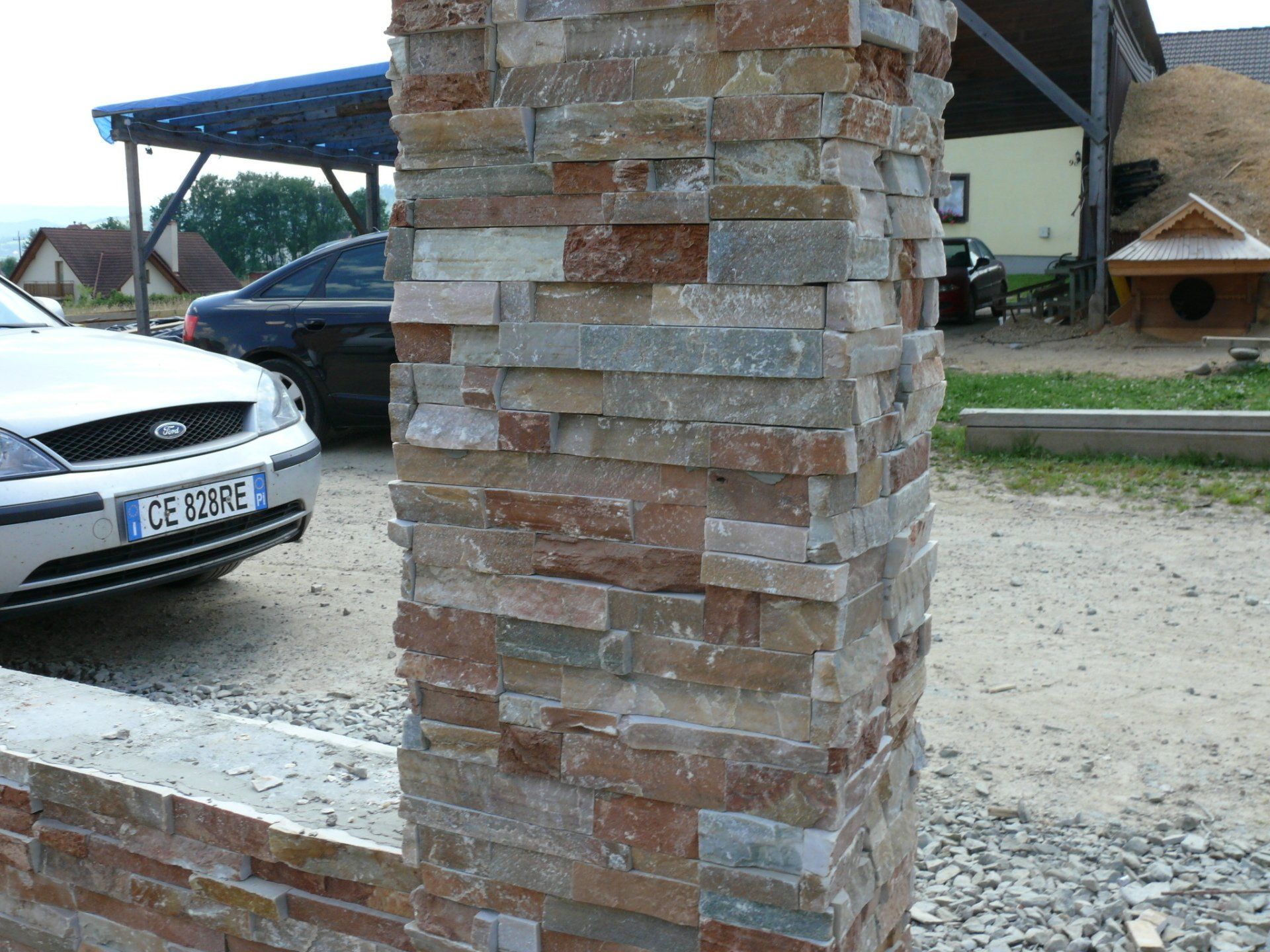 Kamienna kolumna z wielokolorowym, ułożonym warstwowo wzorem z cegieł, na zewnątrz, w pobliżu samochodów i budynku.