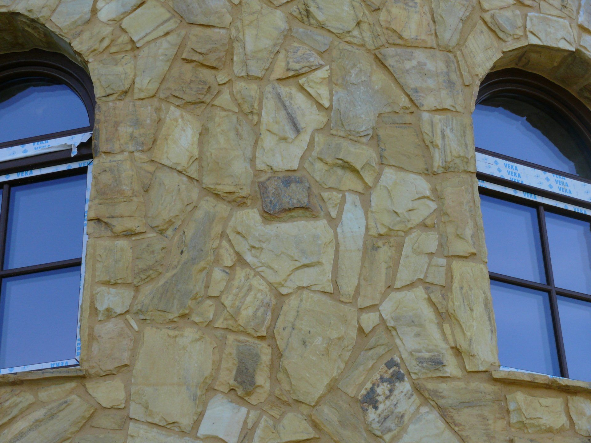 Dwa łukowe okna z ciemnymi ramami na kamiennej ścianie.