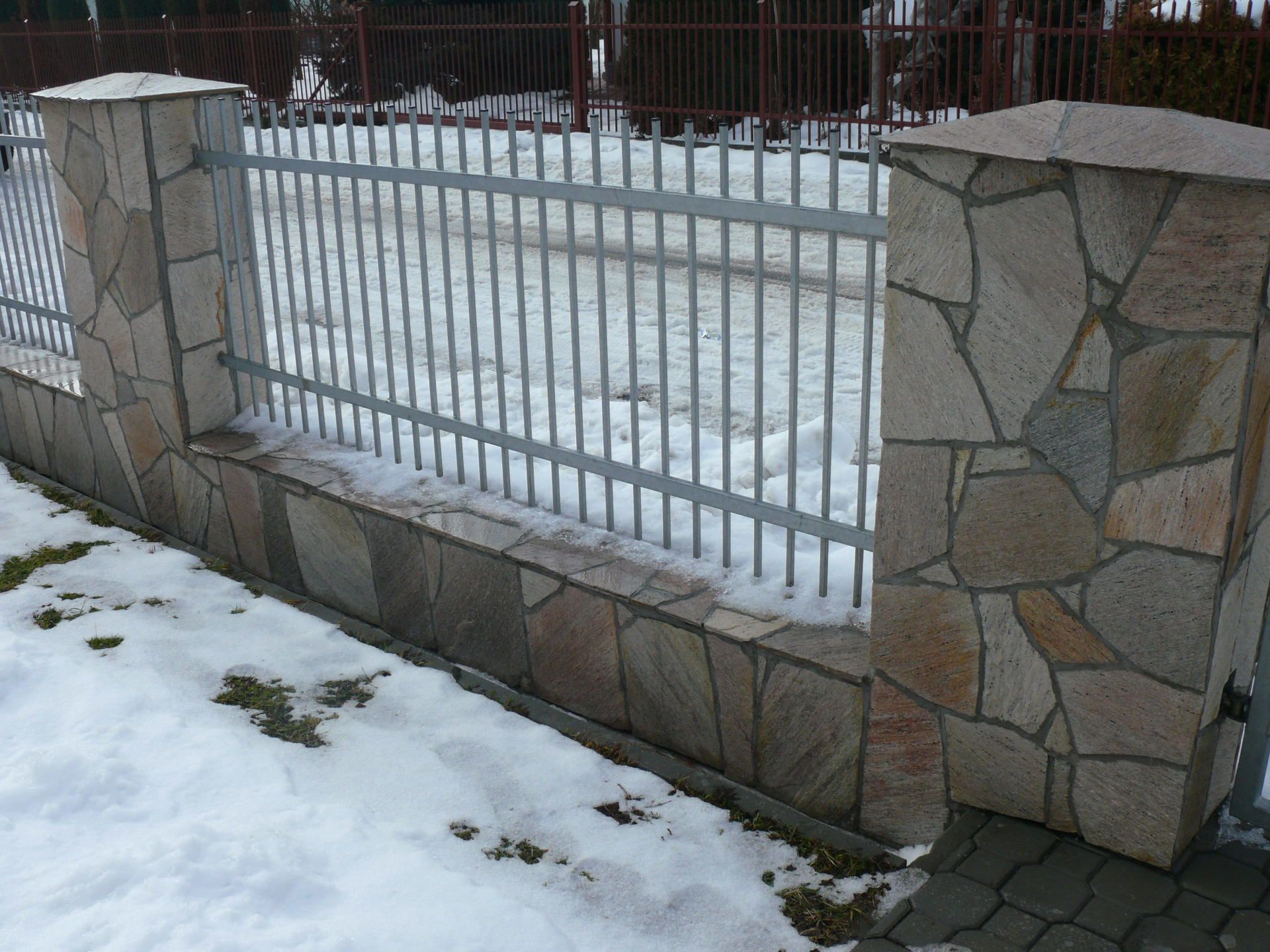 Kamienny płot z metalowymi prętami. Ziemia pokryta śniegiem.