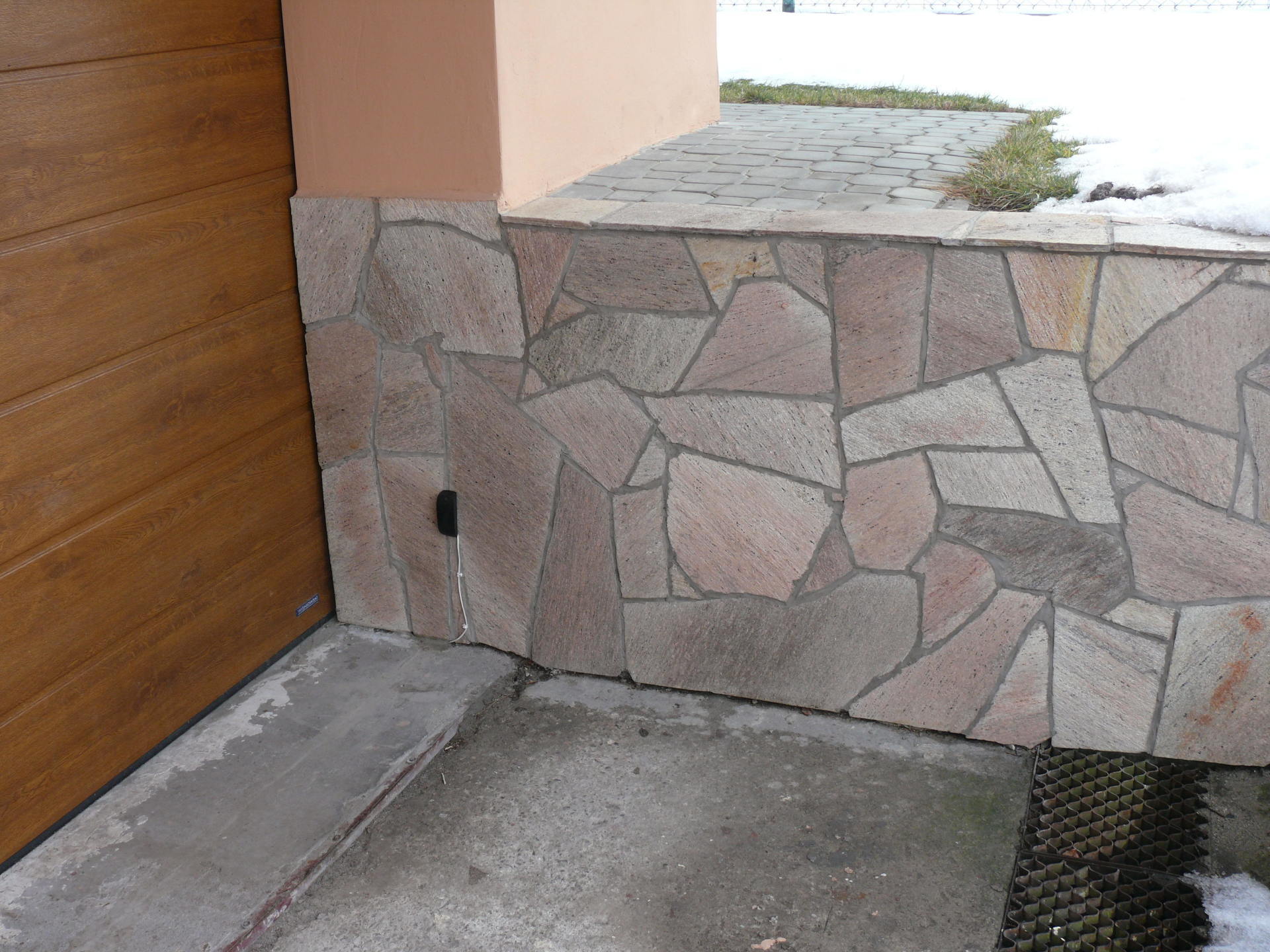 Kamienna fasada z betonową podłogą przed drewnianymi drzwiami.