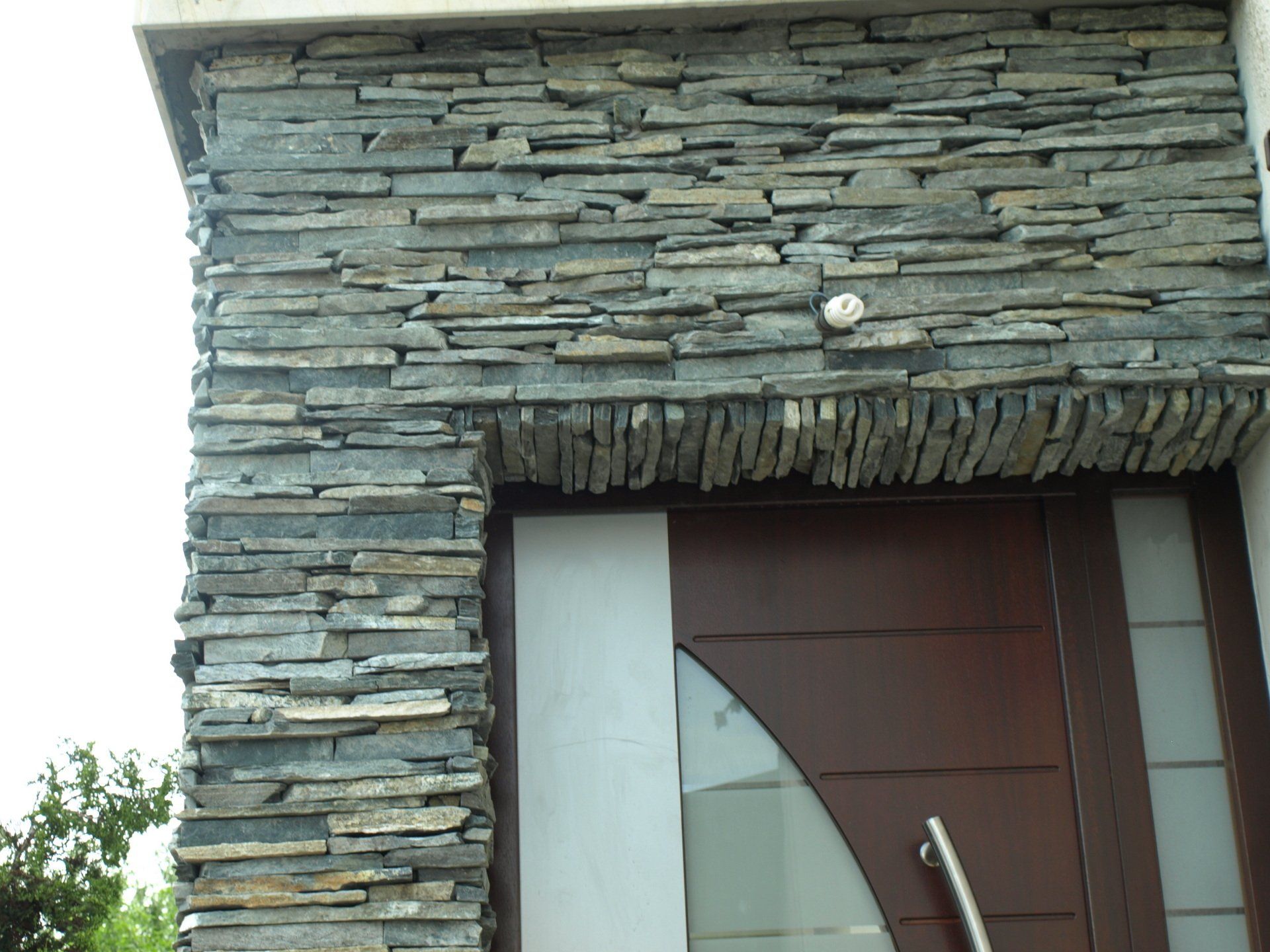 Kamienna elewacja wejścia z brązowymi, drewnianymi drzwiami. Szary kamień otacza framugę drzwi.