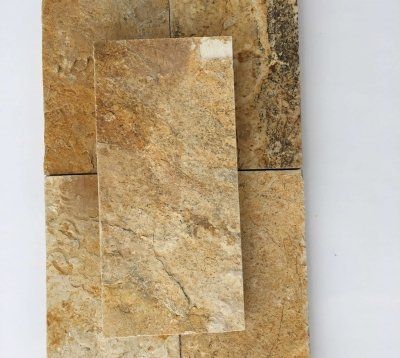 Zbliżenie złocisto-brązowych płytek kamiennych o chropowatej, teksturowanej powierzchni, ułożonych na białej powierzchni.