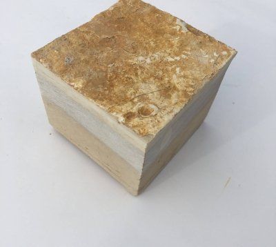 Sześcienna skała osadowa z widocznymi warstwami, brązowa i jasnobrązowa, leżąca na białej powierzchni.