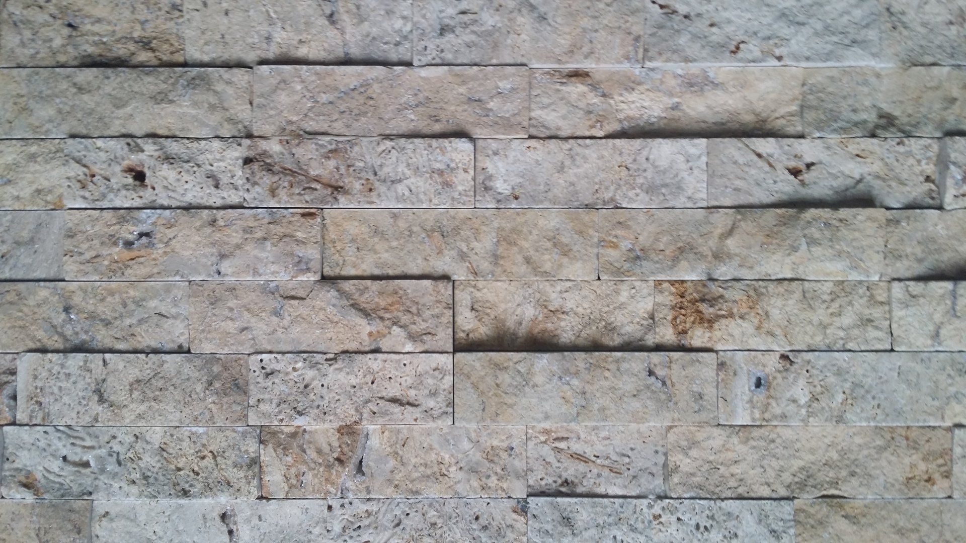 Zbliżenie ściany z jasnymi, prostokątnymi płytkami kamiennymi ułożonymi w sposób przesunięty.