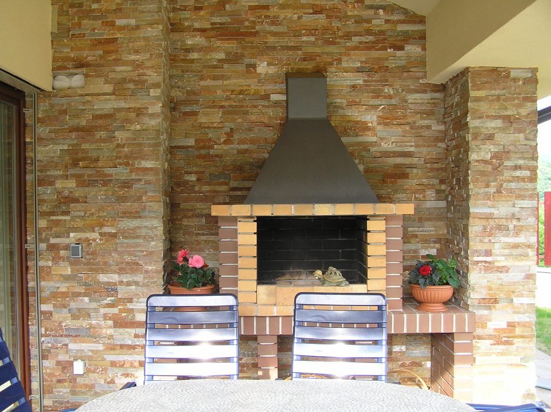 Murowany grill ogrodowy z metalową osłoną, otoczony ceglanymi kolumnami i dekoracyjnym kamiennym murem.