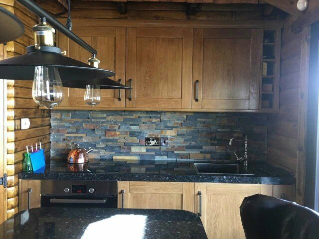 Kuchnia z szafkami z jasnego drewna, kamiennym panelem ściennym, czarnymi blatami i czarnym zlewem.