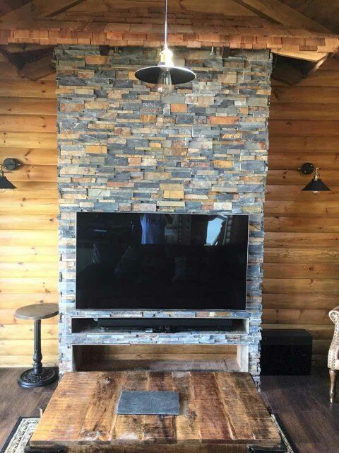 Kamienny kominek z zamontowanym telewizorem, drewniane ściany i rustykalny stolik kawowy.