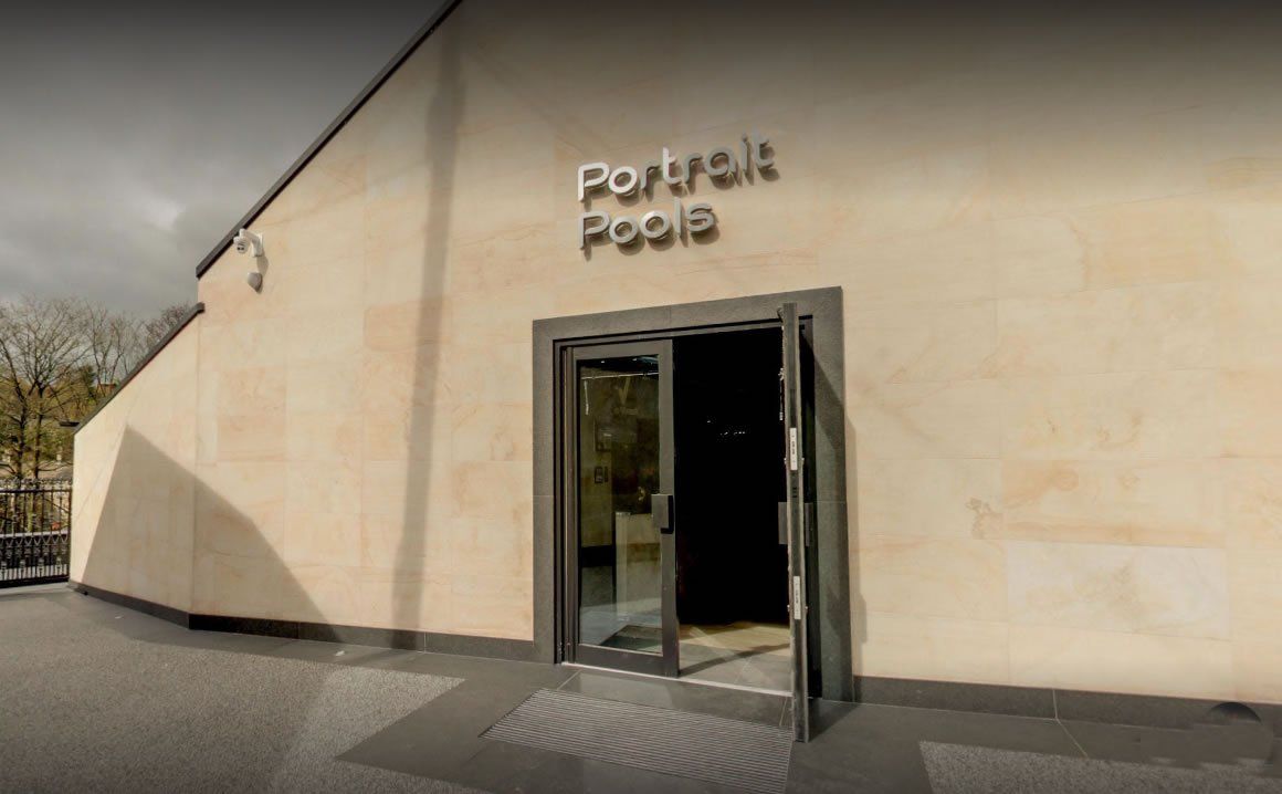 Wejście do Galerii Portretów z otwartymi szklanymi drzwiami i tablicą informacyjną.