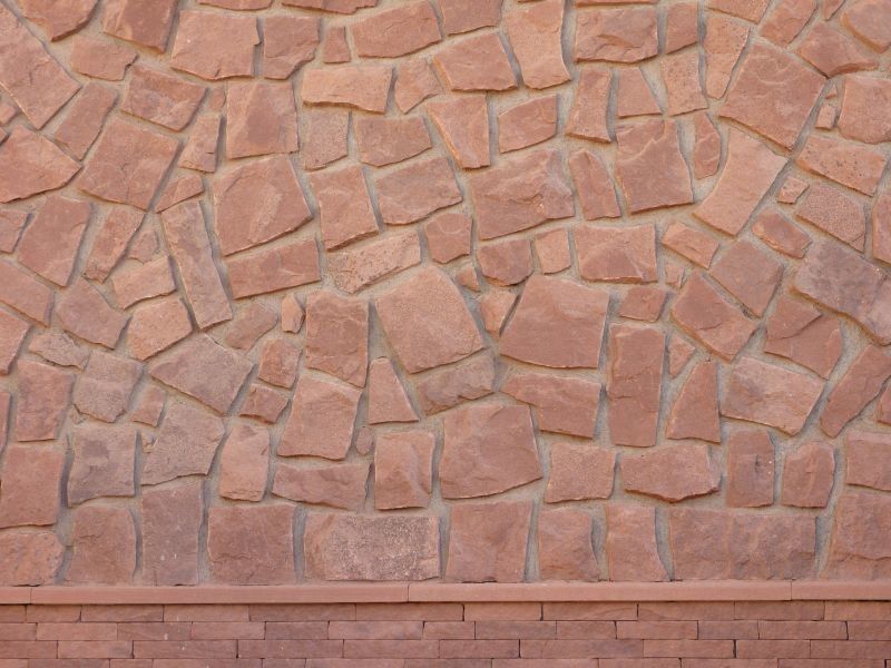Brązowy kamienny mur o nieregularnym, fakturowanym wzorze i dolnej granicy z mniejszych, podobnych kamieni.
