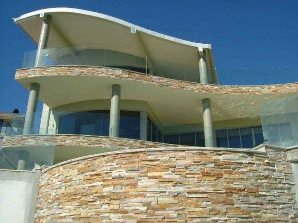 Nowoczesny dom na plaży z zakrzywionym dachem i kamienną fasadą.