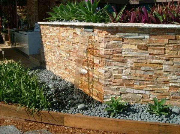 Kamienny element wodny z roślinami u góry i szarym żwirem poniżej.