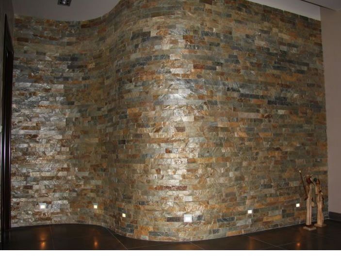 Kamienna, zakrzywiona ściana wewnętrzna z oświetleniem wpuszczanym. Ziemiste odcienie, brąz i beż, tworzą wizualną fakturę.